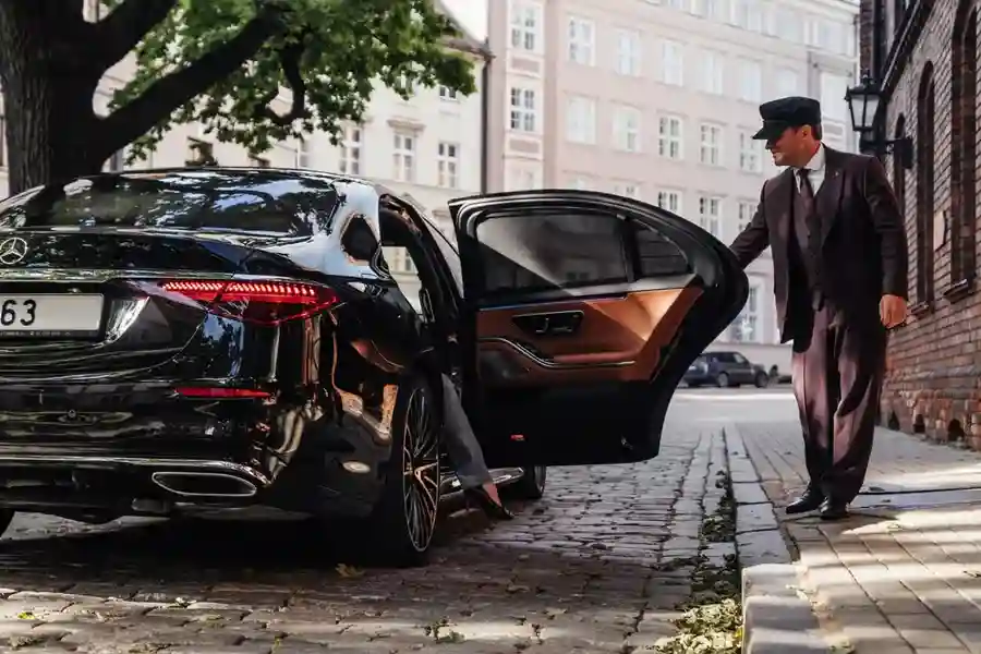 Symbolizing luxury transportation from Houston to Galveston, a professional chauffeur opens the door of a sleek black Mercedes S-Class as a stylish woman arrives at her upscale destination.